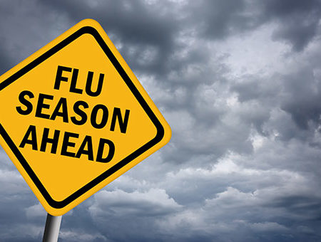 Photo of yellow road sign against gray cloudy sky that says flu season ahead