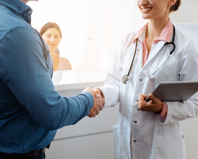 White doctor and white patient shaking hands at front desk of doctor's office.