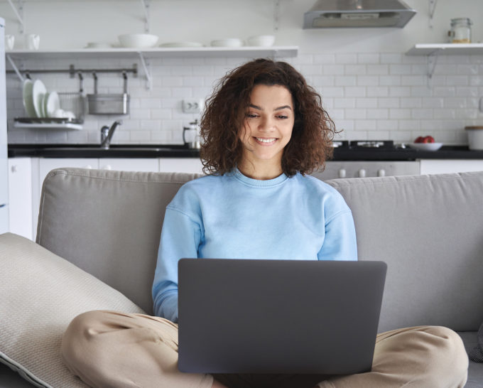 Happy hispanic teen girl holding laptop computer device technology sitting on couch at home.
