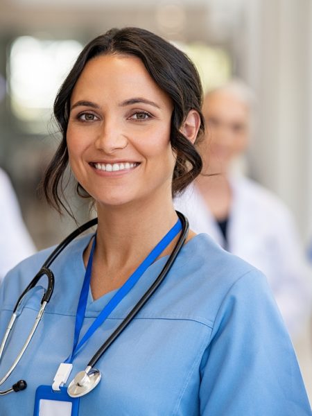 Portrait of happy young nurse in uniform with healthcare team in background. Successful team of doctor and nurses smiling. Beautiful and satisfied healthcare worker in private clinic looking at camera