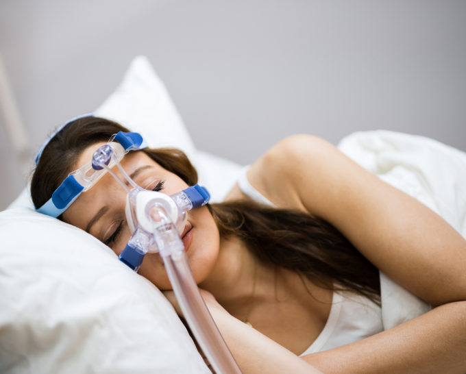 Woman sleeping while wearing a sleep apnea oxygen mask equipment connected to CPAP machine | Granville Health System