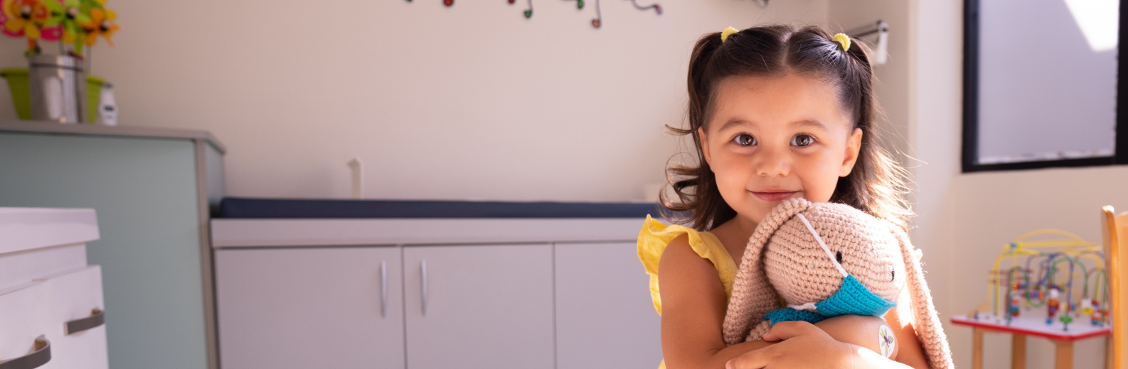 Young girl smiles at camera while holding a stuffed bunny in a pediatric office