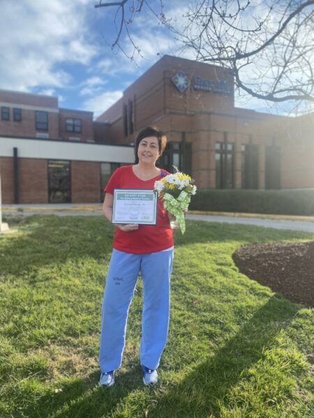 Crystal Paynter, RN and 4th Quarter DAISY Award Honoree, poses with award plaque and flowers