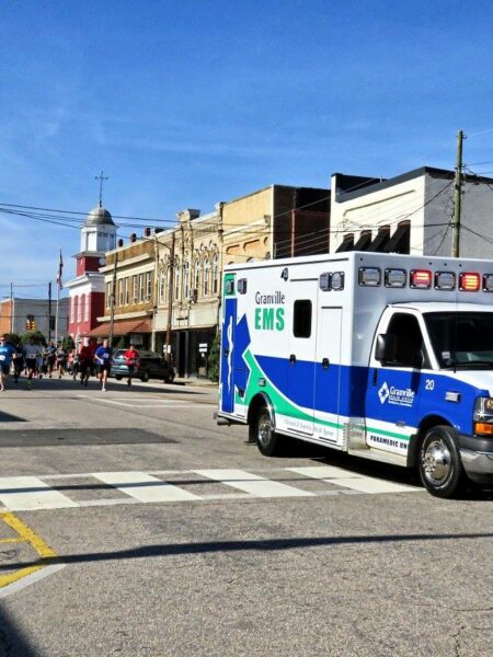 Ambulance on Main Street driving forward while Ambulance Chase participants run behind it.